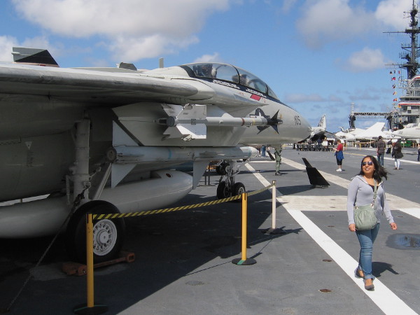 Lady walks past F-14 Tomcat fighter jet on USS Midway aircraft carrier's flight deck.