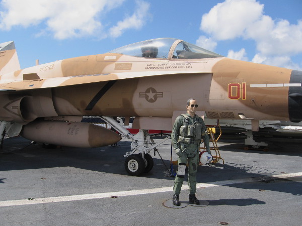 Navy pilot mannequin in flight suit stands near FA-18 Hornet, painted as a TOPGUN enemy aircraft.