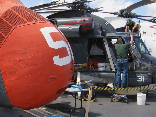 Volunteers work to restore SH-2 Seasprite, beyond orange nose of H-34 Seabat.