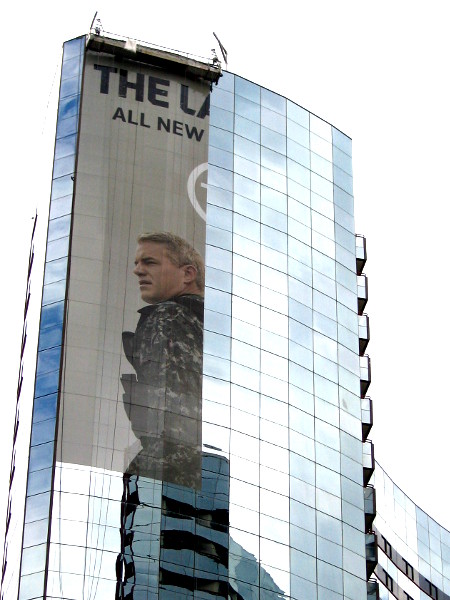 A suspended platform is used to adhere panels of a The Last Ship building wrap to windows of the shining Marriott Marquis.