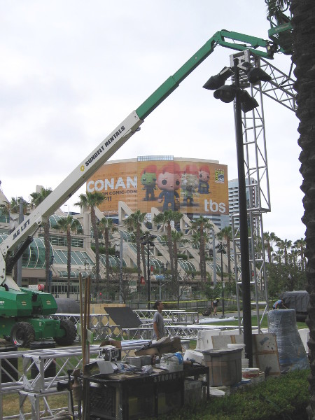 Conan O'Brien building wrap is visible beyond crane erecting framework of Assassin's Creed obstacle course.