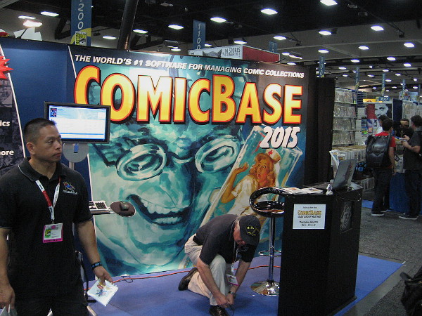 Sinister face on large ComicBase software graphic seems to be looking down at an exhibitor as he ties his shoelace!