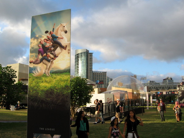 Folks riding a unicorn prepare to launch above the Omni Hotel into the cloudy blue sky, over a gigantic bubble resting on the grass!