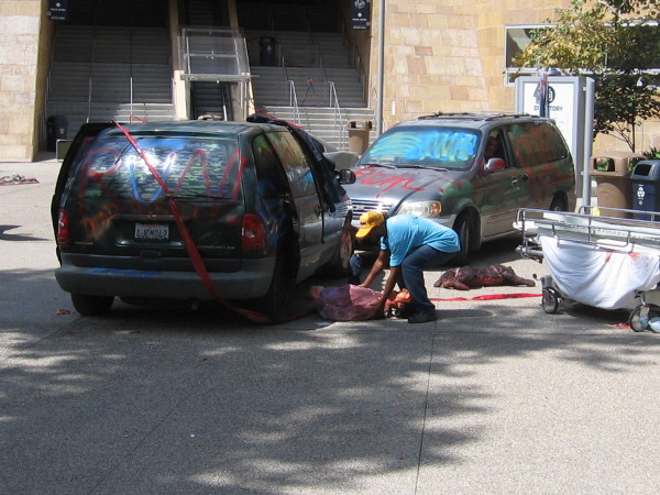Guy places a dummy corpse by a bloody, crashed car.