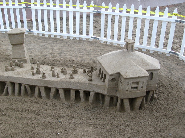 A second photo of Kirk Rademaker's sculpture. Tiny sand people stand out on a sand IB pier over the sandy Pacific Ocean!