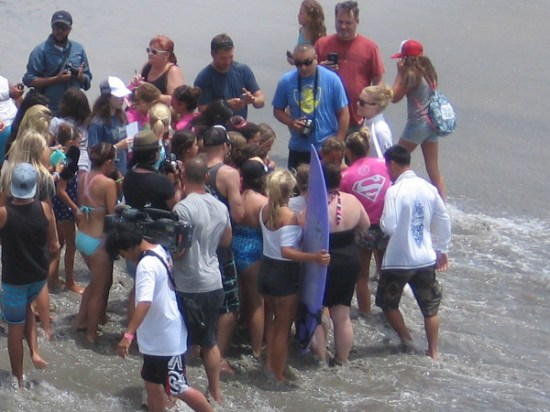 I see a pink Supergirl cape on one superheroic surfing celebrity! The event is in part sponsored by DC Comics, where the fictional character was born.