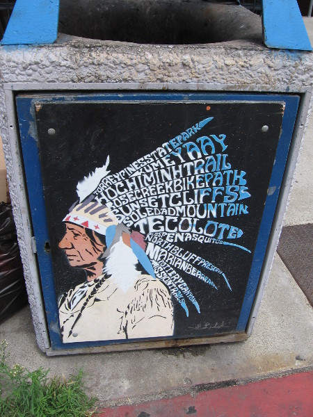 Trashcan street art depicts Native American, whose headdress contains feathers spelling place names.