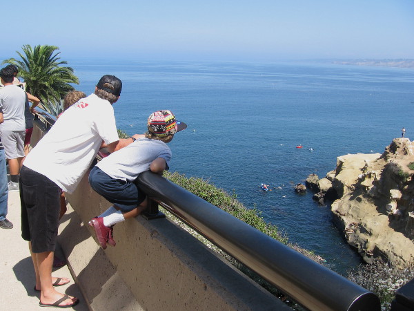 It's a beautiful day by the ocean in La Jolla. Some kayakers have noticed the entrance to a sea cave in the sandstone. Curious eyes spot them from above and watch the unfolding drama.