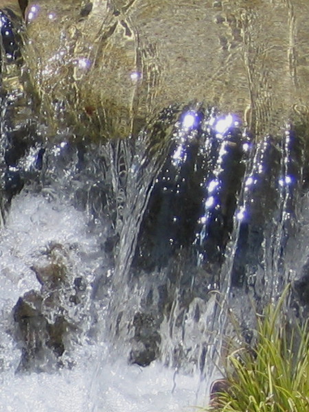 Water cascading over stone shines in the sunlight. A small happy river flows through the bottom of the spacious garden canyon.