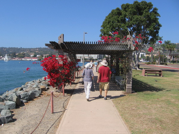 People walk along the pathway which stretches down narrow Shoreline Park. Grass, benches and picnic tables invite both locals and tourists.