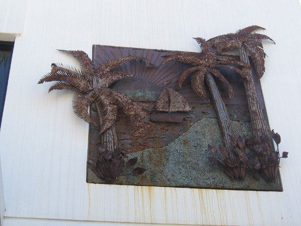 Some interesting metal artwork above a store entrance depicts a sailboat and palm trees.