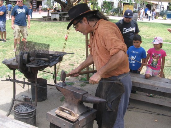 A patient blacksmith bangs away on some hot metal as he fashions a thin, pointed nail.