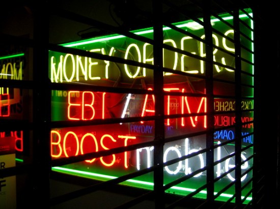 Neon words and their reflections broken up by a security grill in front of one store.