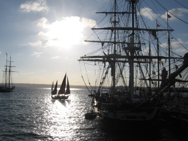 Sailboat on a puddle of light behind the tall ship Pilgrim, as day ends at the Festival of Sail on San Diego's Embarcadero.