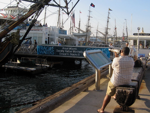 Photographer near the HMS Surprise takes photos of many masts along the waterfront beyond the Maritime Museum of San Diego.