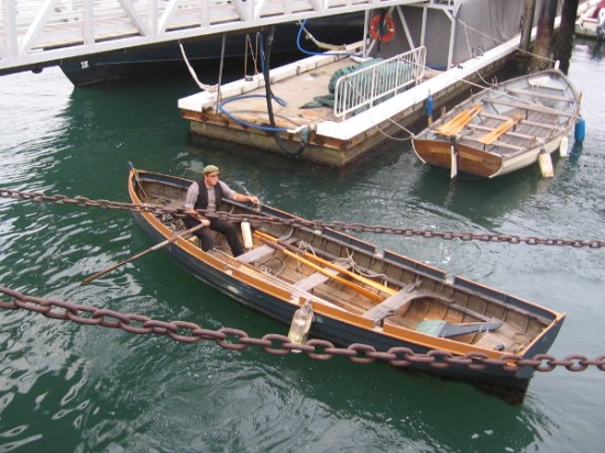 Gentleman from the Maritime Museum rows a longboat under ramp which leads to the HMS Surprise and other historic ships on San Diego Bay.
