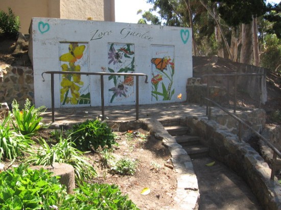 Sunlight reflects from a butterfly winging past some weathered public art in a section of the garden.