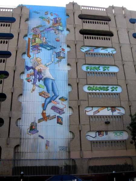 A human connected to technology in this new public art mural. Park it, charge it! The seven-story parking garage is located at 707 Broadway. This photo was taken from 7th Avenue.