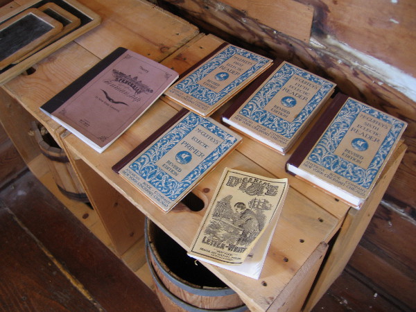 Some old Primers and Readers on a wooden table. A water bucket and dipper were used for drink.
