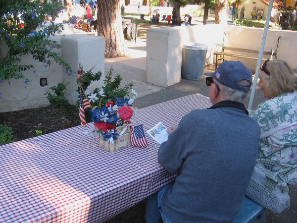 Folks at a table in front of the House of USA Cottage listen to the band play patriotic and other popular tunes.