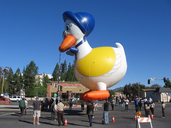 An inflatable Mother Goose balloon floats in the blue sky as the parade is ready to begin.