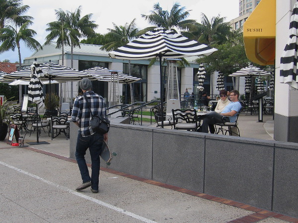 A guy carrying a skateboard ambles past outdoor diners at Sally's Seafood on the Water.