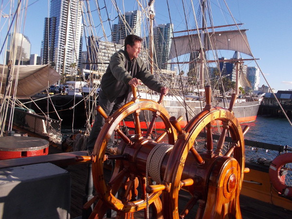 Visitor to the San Diego Maritime Museum pretends to steer the amazing tall ship, which is docked on the Embarcadero near the historic Star of India, in the background.