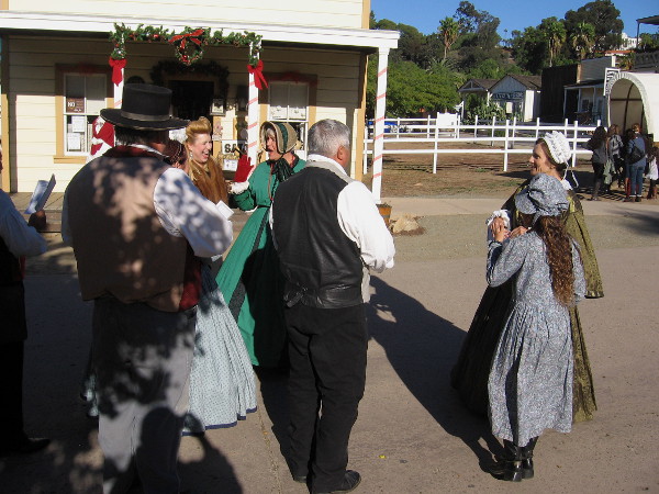 Carolers smile, laugh and enjoy the day in front of a reconstructed building at Old Town San Diego's central plaza.