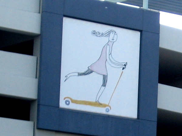 A carefree girl rides a scooter on the side of the North Park parking garage.