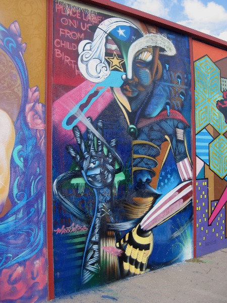 Spray paint art by San Diego artist Maxx Moses. A character composed of many diverse elements, beneath the words Place Labels on Us From Childbirth.