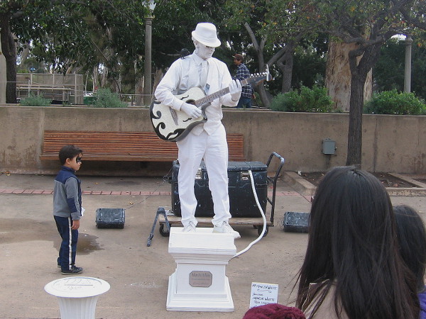 Kid with painted face examines Man in White. This cool busker appears to be made of marble. He was entertaining surprised visitors on El Prado.