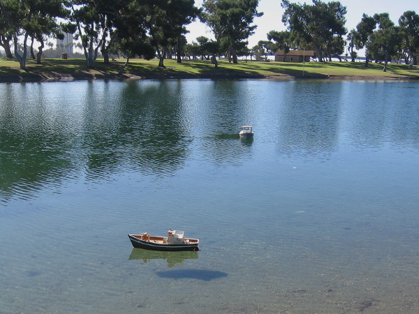 Two electric-powered model boats navigate by radio control across the smooth pond.