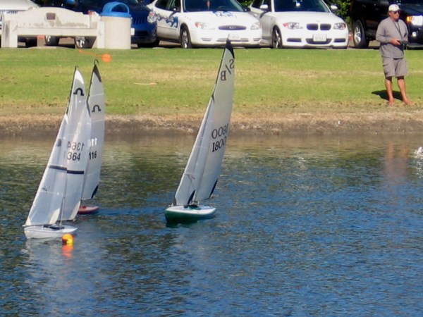 Three model sailboats tack to go around a tiny buoy.