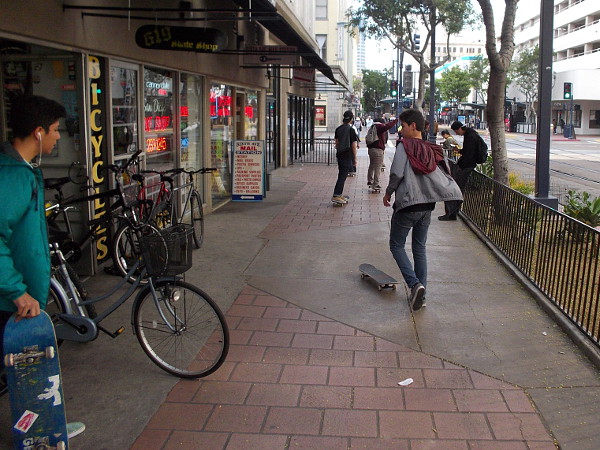 A group of young skateboarders cruises down C Street.