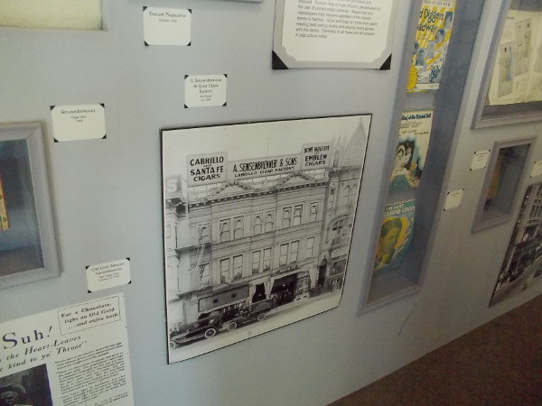 On the wall are many historical photos and artifacts, including an image from around 1930 of a cigar factory on 4th Street in San Diego.