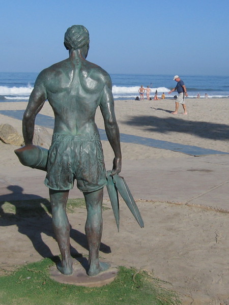 The muscular bronze lifeguard statue holds a rescue tube and a pair of swim fins