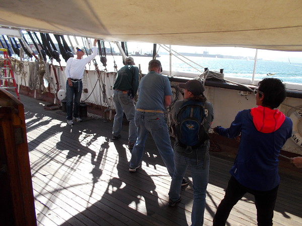 Volunteers at the Maritime Museum of San Diego haul a rope on the deck of Star of India to help raise a protective tarp above the historic ship.