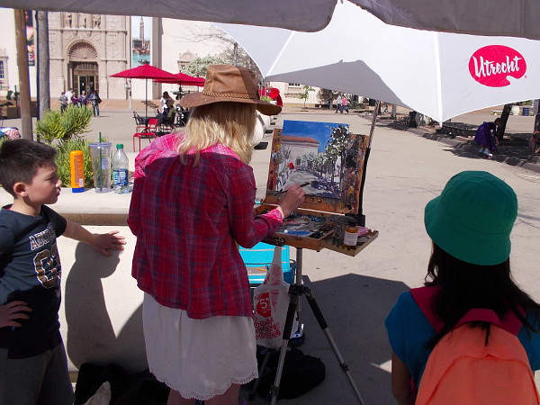 Young people were watching a lady artist paint a scene in Balboa Park.