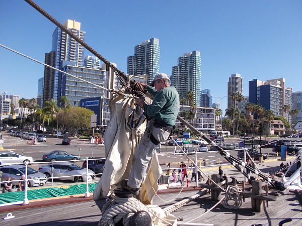 Another volunteer works near the bow of the historic tall ship. Downtown San Diego's skyline provides a gleaming backdrop.