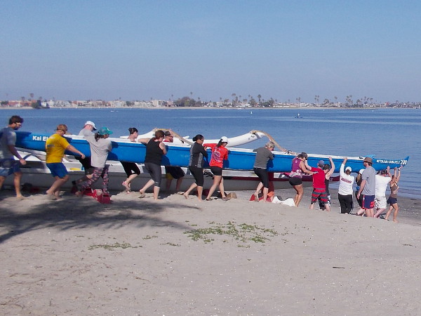 Members and guests of San Diego's Kai Elua Outrigger Canoe Club carry an outrigger canoe across the beach toward the water of Mission Bay.