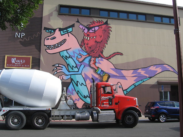 Funny urban art in North Park. A cool T. rex and fuzzy rider rise high above a concrete mixer truck. Created by artist Mark Paul Deren, also known as Madsteez.