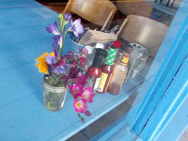A peek through a window at flowers on a table inside a Little Italy breakfast spot.