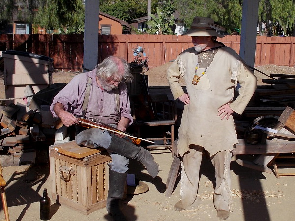 Two rugged mountain men, one with a fiddle, hang out behind Seeley Stable at Old Town San Diego State Historic Park.