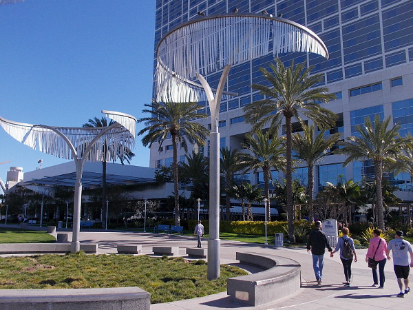 People walk beneath unique tree-like art between the San Diego Convention Center and the Hilton hotel.