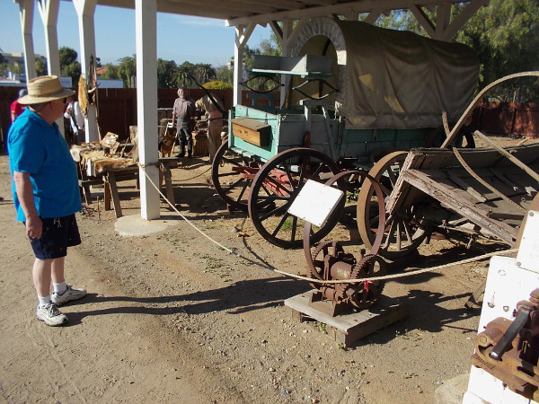 Someone reads a sign near a tyre bender. This device was used to send long, flat bars of iron or steel into a smooth circle that would become an iron tyre.
