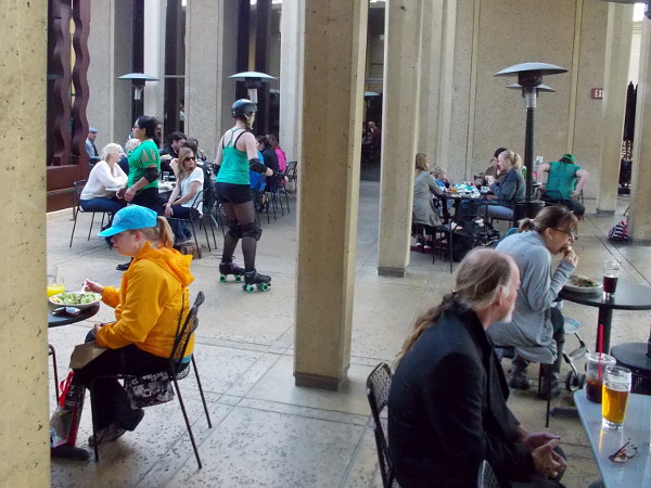 A park visitor on roller skates passes through the May S. Marcy Sculpture Court while diners at Panama 66 enjoy life.