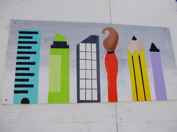 A skyscraper joins the ranks of a vertical pencil, ruler and paint brush.