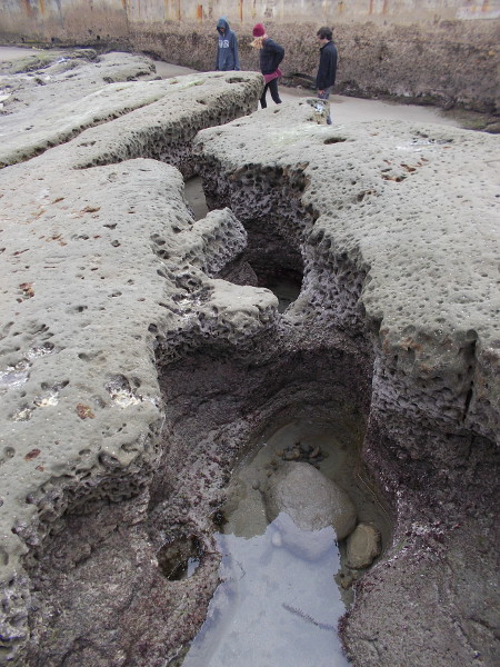 Kids stand near the sea wall at the end of one water-sculpted, crevice-like channel.