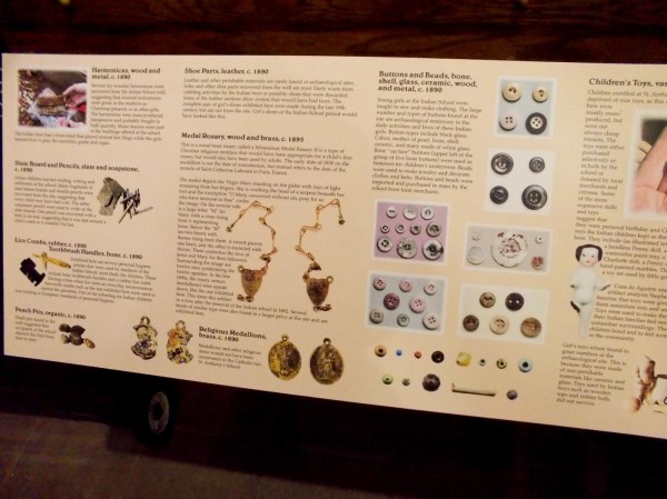Sign describes additional historical finds, including buttons, toys, harmonicas, slate board and pencils, lice combs, toothbrush handles, shoe parts, medal rosary and religious medallions.