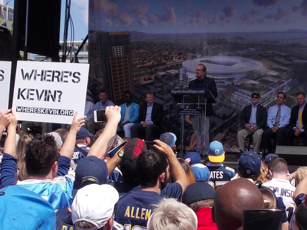 Dean Spanos, team president and CEO of the National Football League's San Diego Chargers team takes the stage. Pre-made signs intended to shame Mayor Faulconer rise in unison.
